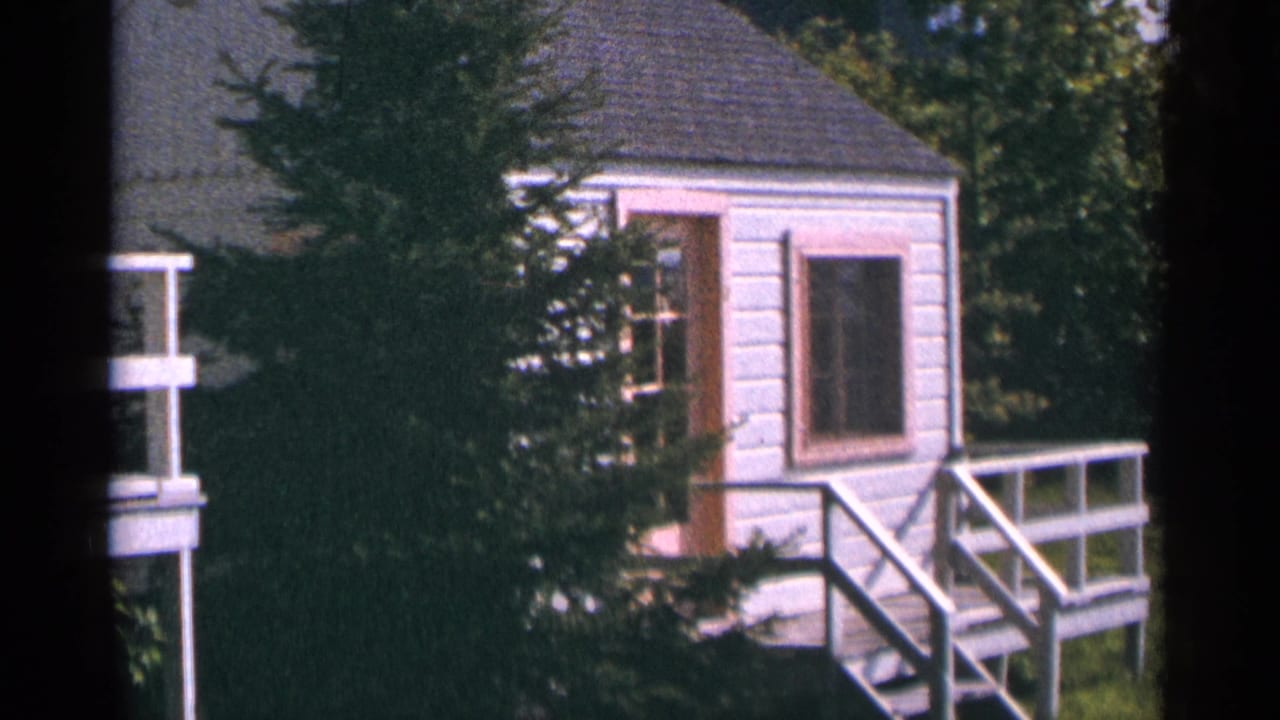 Cabin exterior and deck seen through trees in soft 8mm color.