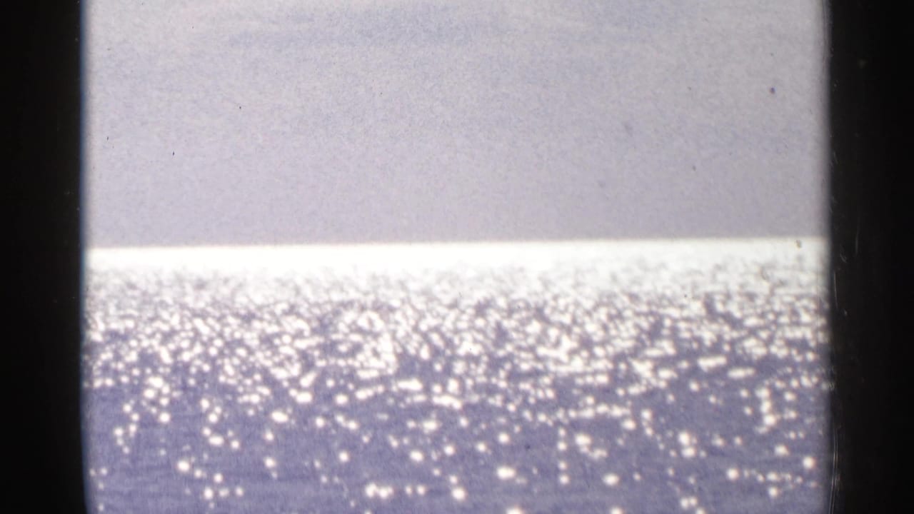 1964 Minnesota 8mm frame showing sunlight glittering across open lake water beneath a pale sky or distant shore.