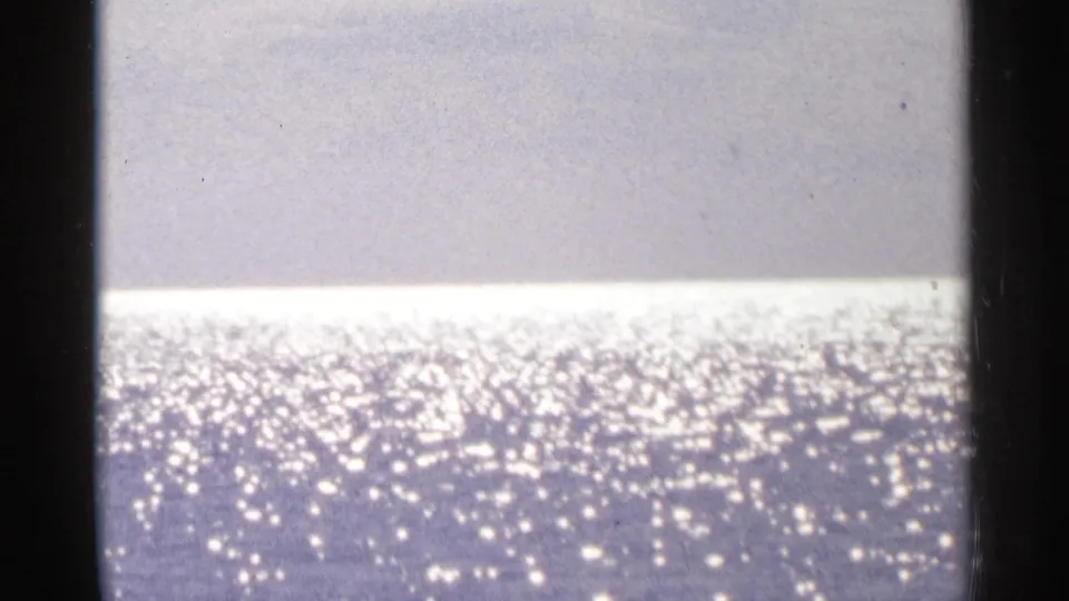 1964 Minnesota 8mm frame showing sunlight glittering across open lake water beneath a pale sky or distant shore.
