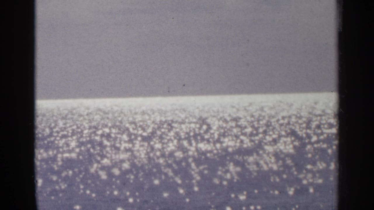 Minnesota 1964 home-movie frame focused on glittering lake water, with a muted horizon and visible film texture.