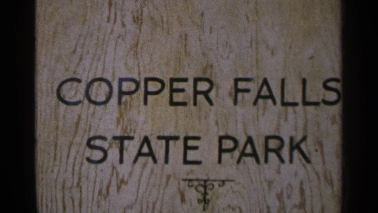1964 home-movie frame centered on the Copper Falls State Park sign, with soft focus and faded 8mm color.