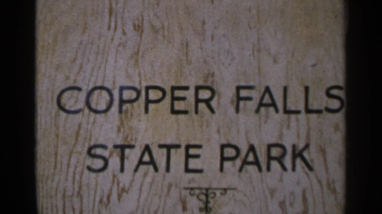Close 8mm frame of the Copper Falls State Park sign, showing black lettering, wood texture, and film-edge darkness.