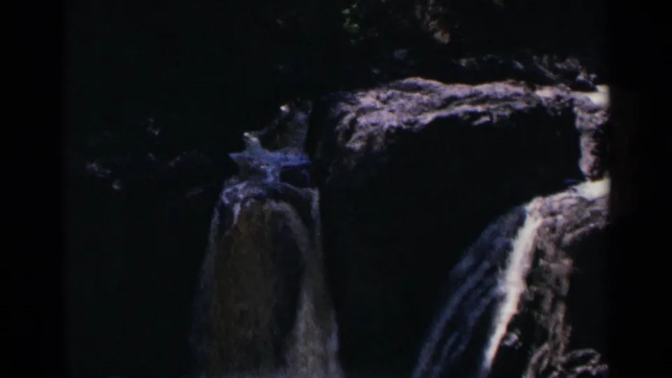 1964 Minnesota home-movie view of a shadowed waterfall dropping over dark rock ledges, with soft focus and visible film borders.