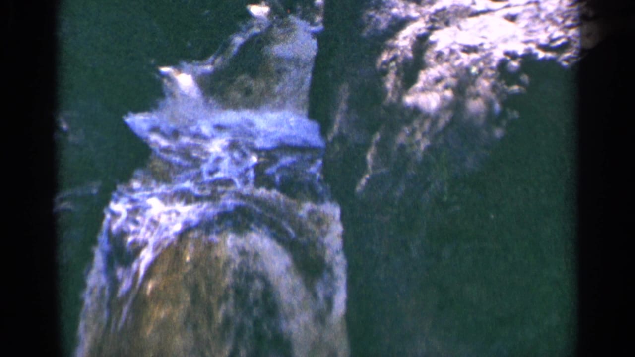1964 Minnesota home-movie close view of foamy waterfall water and adjacent rock, with handheld framing and faded color.