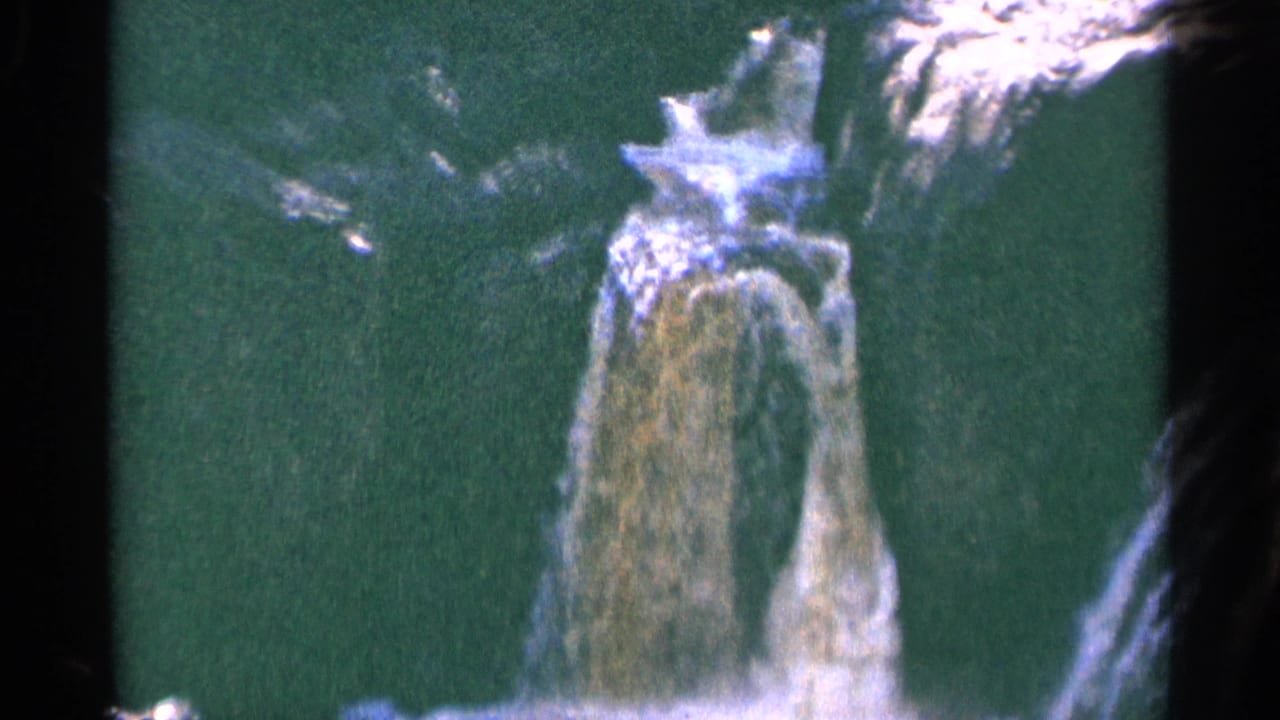 Water drops over a dark rocky ledge into green-tinted water.