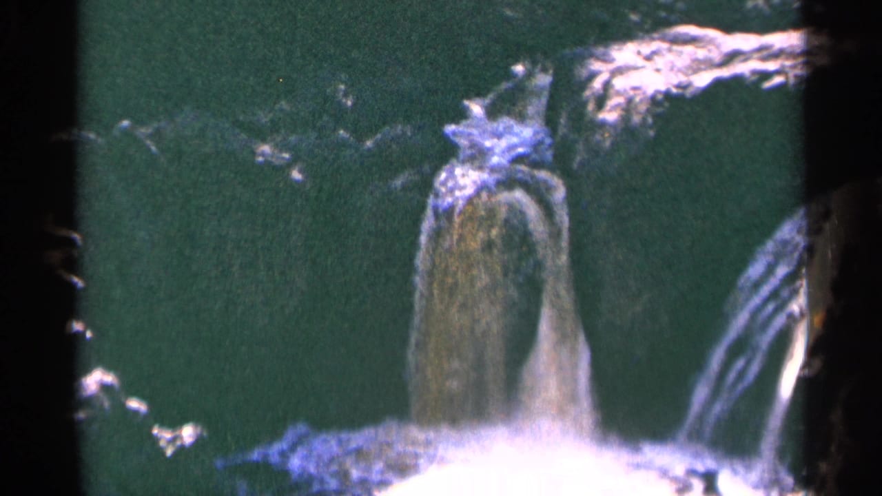 A waterfall pours over rock with a bright splash at the lower edge.