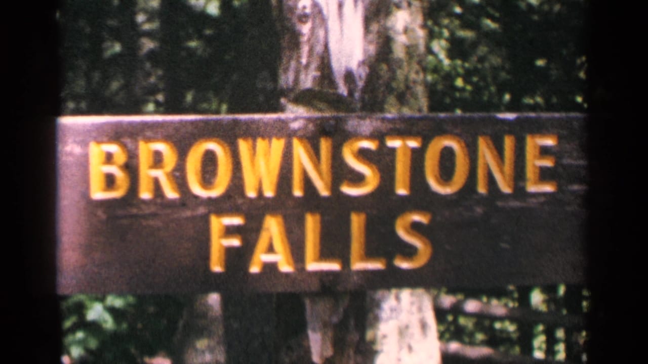 The Brownstone Falls sign remains centered in a 1964 8mm frame, with trees and foliage visible behind the board.