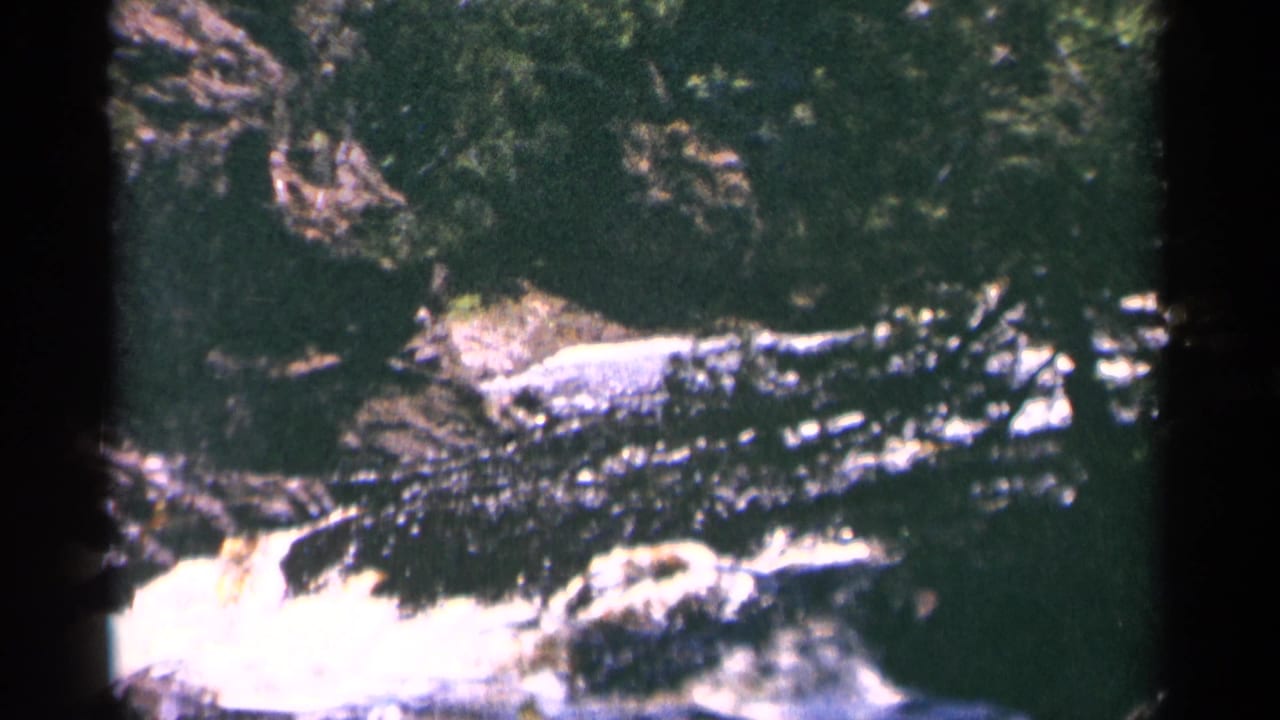 1964 Minnesota 8mm view of whitewater moving over dark rock at Brownstone Falls, with trees and shadowed gorge edges.