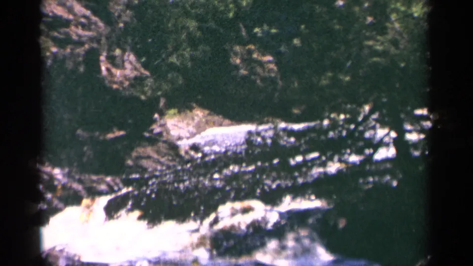1964 Minnesota 8mm view of whitewater moving over dark rock at Brownstone Falls, with trees and shadowed gorge edges.