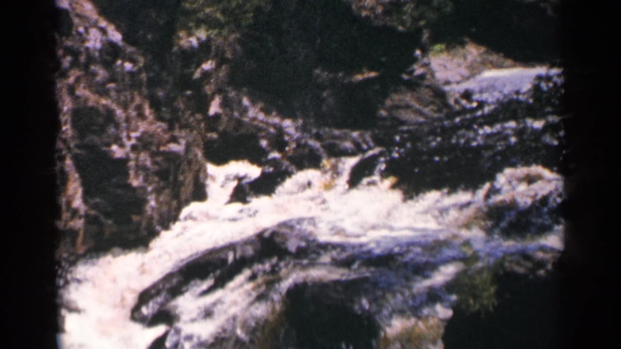1964 Minnesota 8mm frame of foaming current at Brownstone Falls, with rocky gorge walls and dark water channels visible.