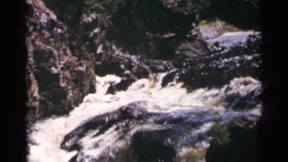 1964 Minnesota 8mm frame of foaming current at Brownstone Falls, with rocky gorge walls and dark water channels visible.