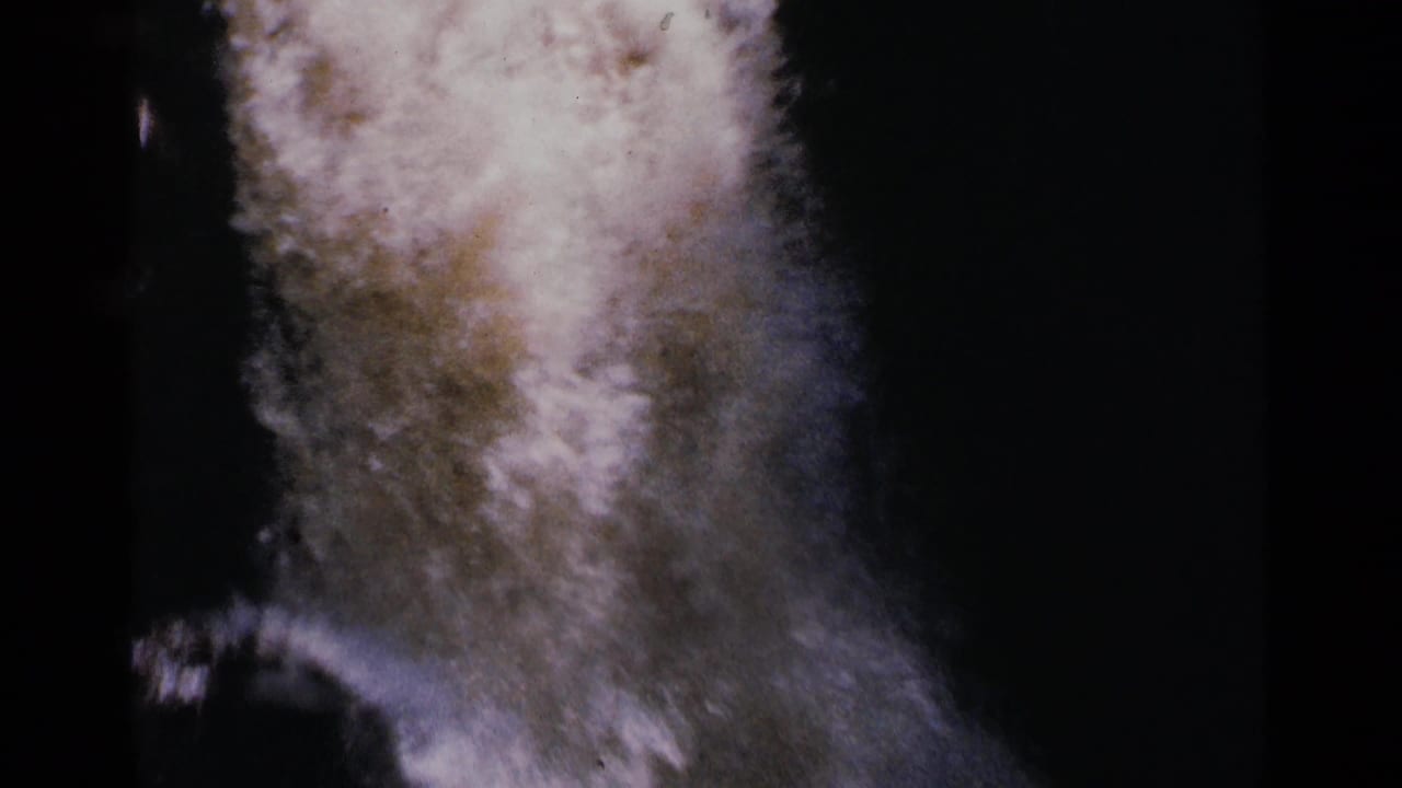 Foamy water rushes through a dark rocky channel in soft 8mm color.