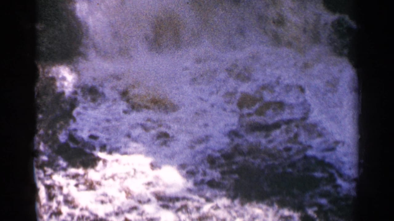 Bright, churning water breaks across dark rocks in a close view.