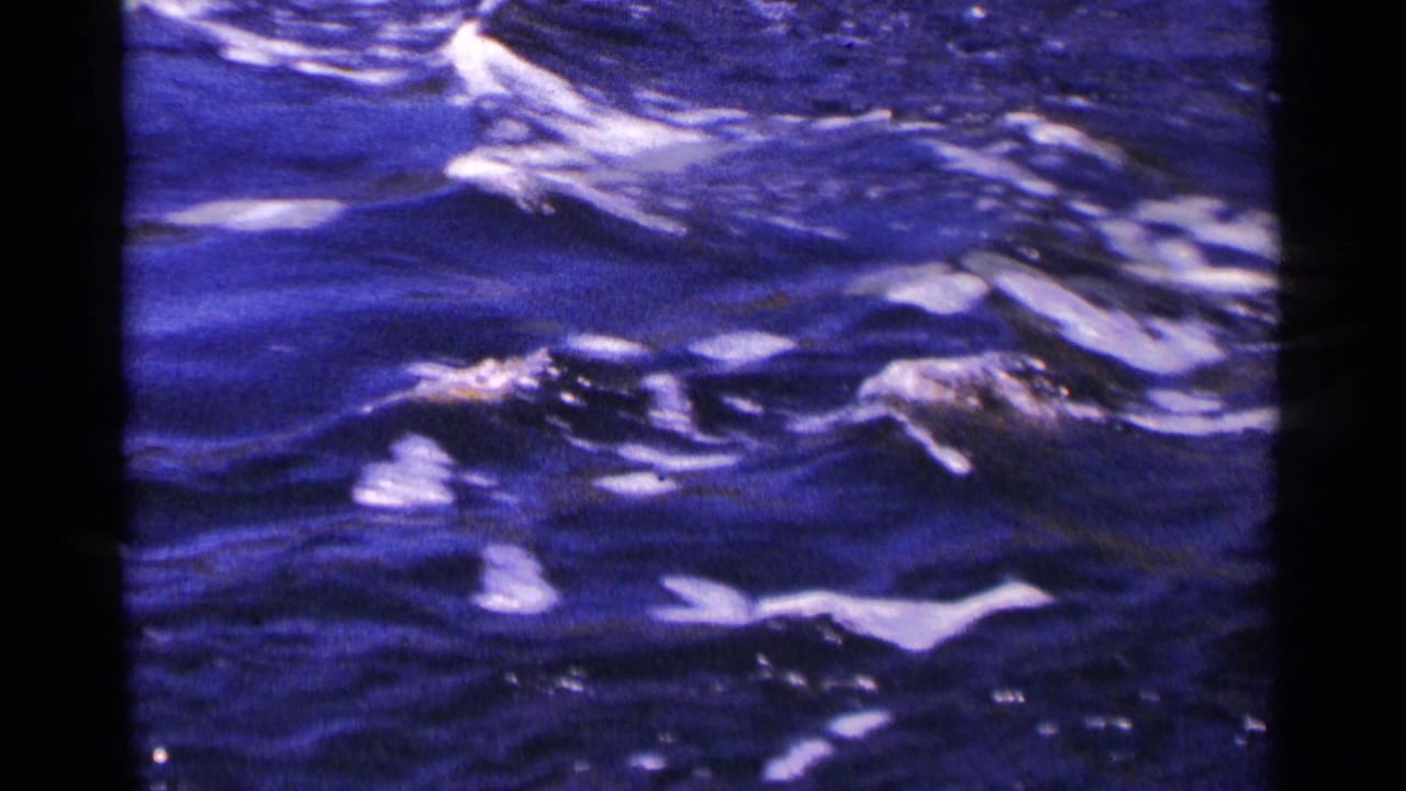 Close 8mm view of fast-moving blue water with bright white reflections and soft film grain.