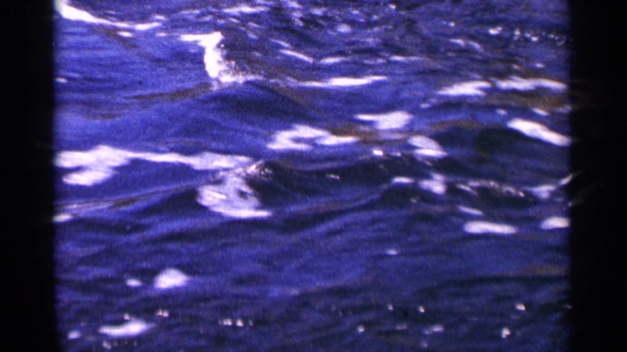 Minnesota home-movie frame focused on rushing blue water, with white highlights and aged-film color shift.