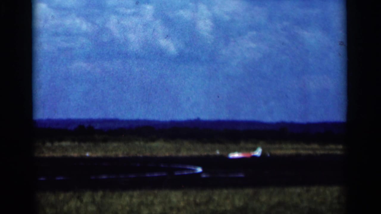A red and white model airplane sits on the open Minnesota airfield in the closing 1964 8mm frame.