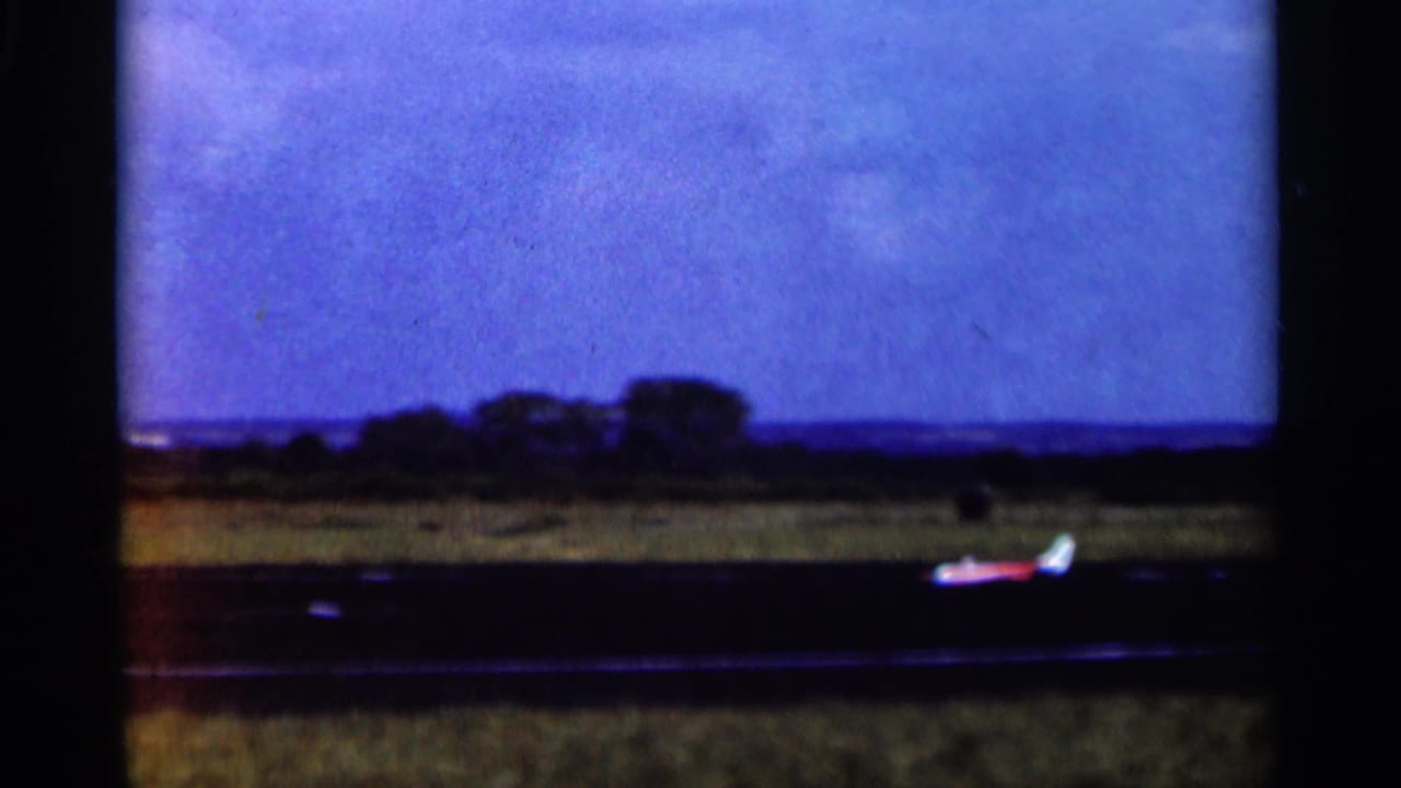 A red-and-white propeller plane remains low near the runway, filmed from a distance at an open Minnesota airfield.