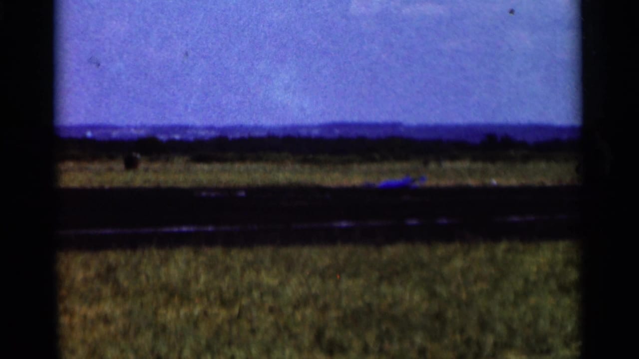 A wide view shows grass, a low horizon, and blue sky near the end of the 1964 Minnesota model-airplane clip.