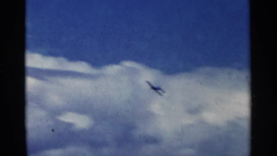 Small aircraft climbs against bright clouds and deep blue sky in 1964 Minnesota home-movie footage.