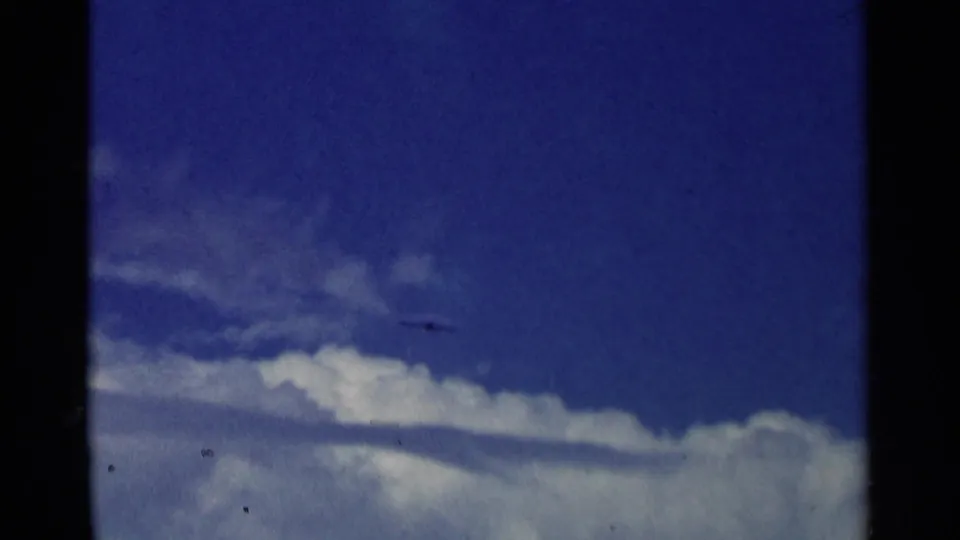 The aircraft appears as a dark shape moving across a cloudy blue sky in the 8mm aviation sequence.