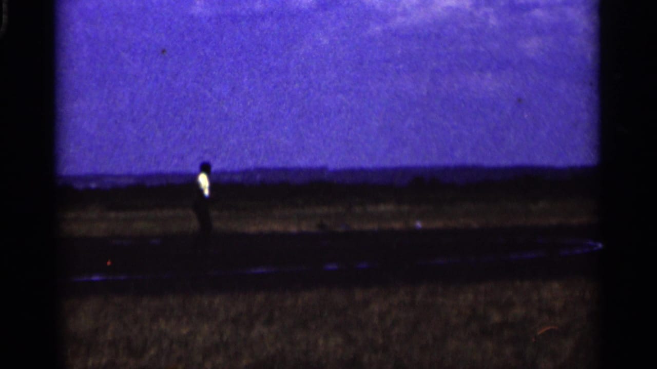 A distant adult figure stands near the grass airfield as the runway and open Minnesota sky fill the frame.