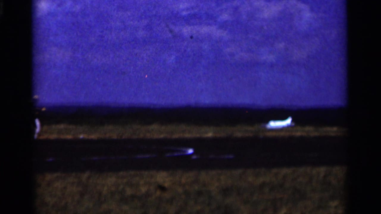 Small white model airplane near a dark strip in an open grassy field.