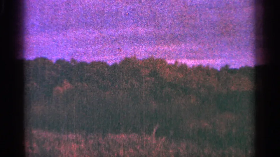 1964 Minnesota 8mm frame of a treeline and field under a mottled purple sky with strong grain.