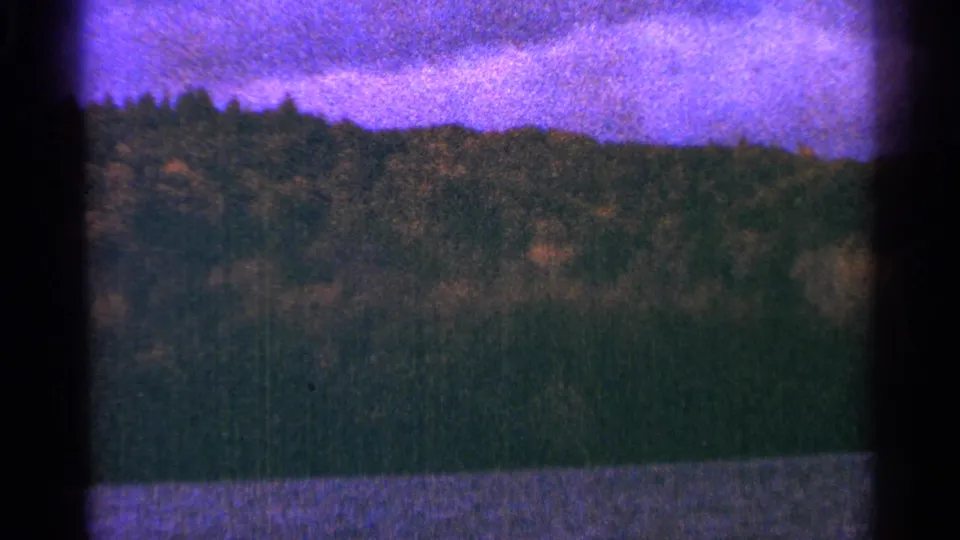 1964 Minnesota 8mm frame showing a tree-covered hill beyond a river edge beneath a pink-purple dusk sky.