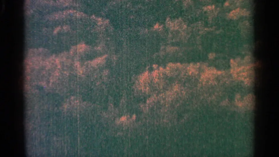 1964 Minnesota home-movie frame showing a darker tree-covered hill with warm foliage near a river or lake edge.