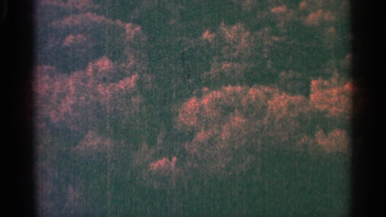 Dark textured landscape-like forms with reddish patches and visible black film borders.