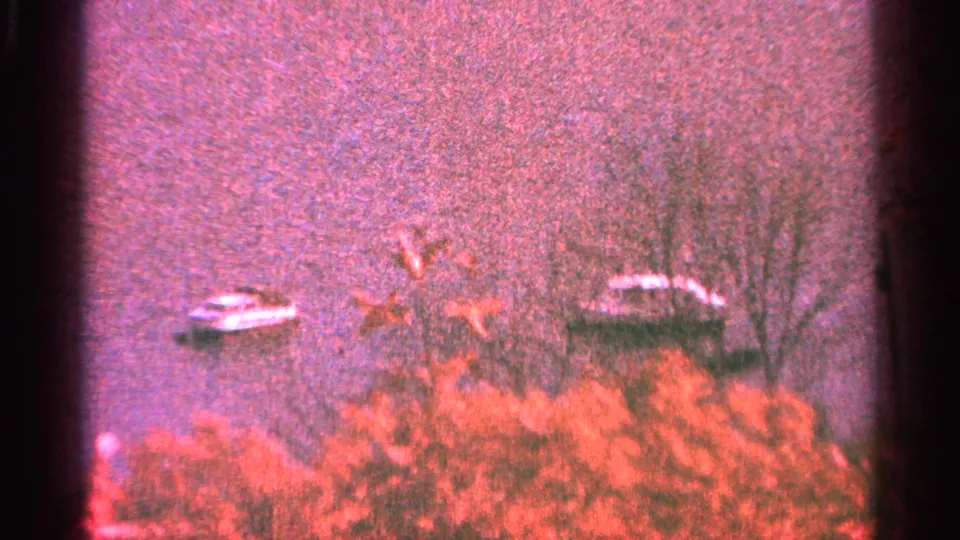 Minnesota 1964 8mm view of two small boats on calm water, partly framed by reddish foliage and leafless shoreline trees.