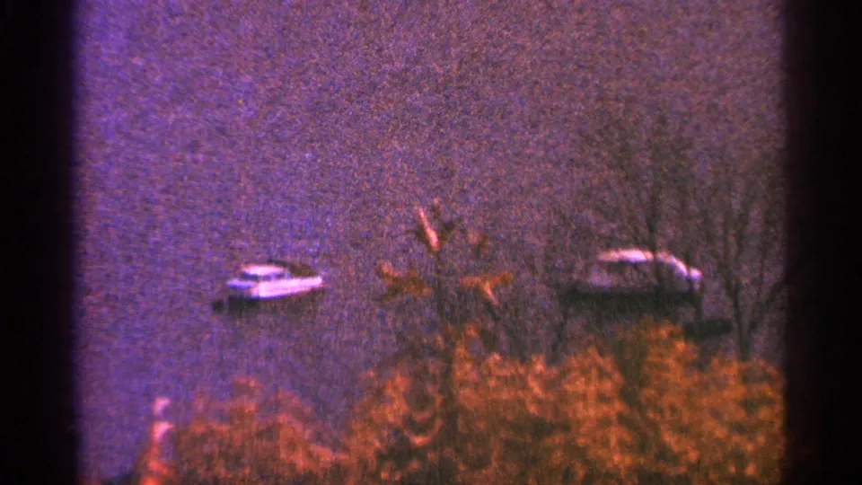 The final frame shows two small boats on purple-toned lake water, with bare trees and reddish shoreline foliage in grainy 8mm color.