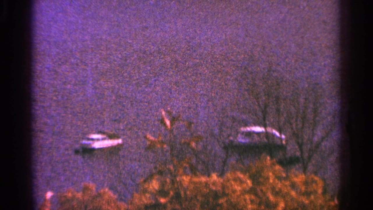 Two small boats floating near a wooded lakeshore with dark film borders.