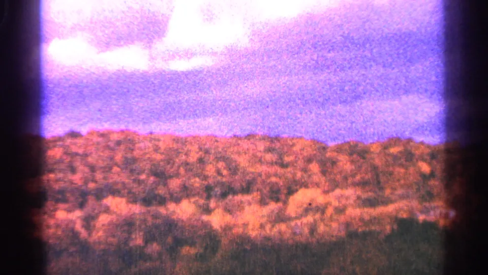 1964 Minnesota 8mm frame showing bright white clouds over a wooded treeline with pronounced pink and purple color shift.