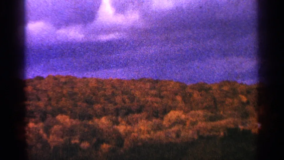 1964 Minnesota 8mm frame showing blue-purple clouded sky above a dark wooded ridge, with heavy grain and gate shading.