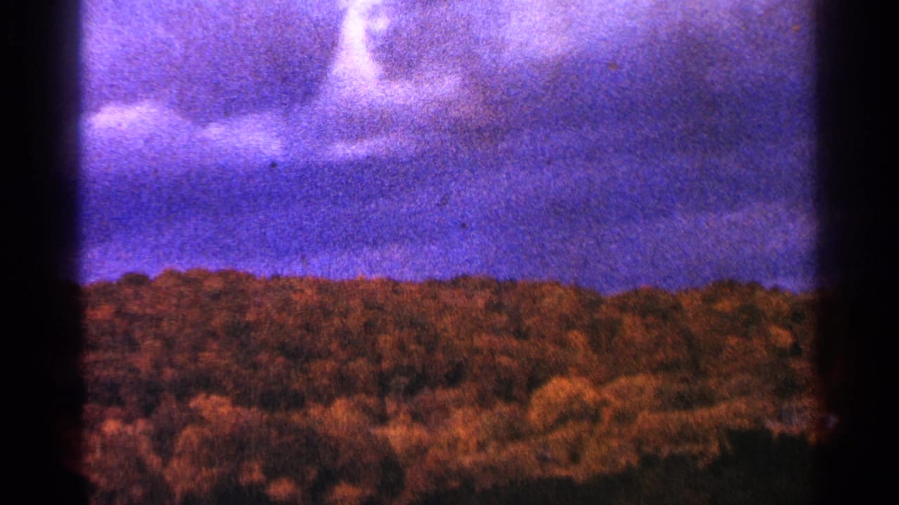 Distant forested ridge under a mottled purple sky with a dark vertical film edge.