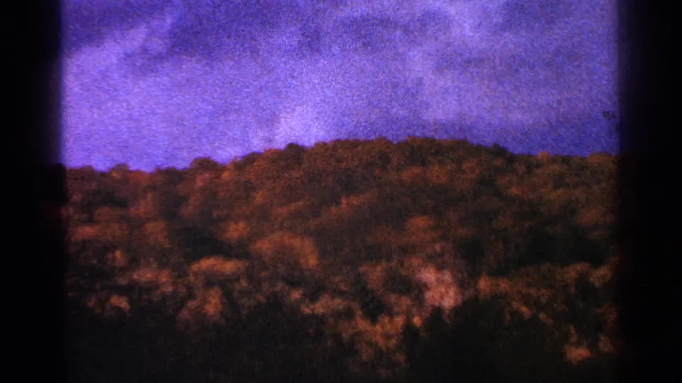 1964 Minnesota 8mm frame showing a soft, grainy wooded hillside under a blue-purple sky with darkened frame edges.