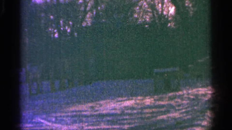 1964 8mm home-movie frame of a snowy Minnesota outdoor scene with dark trees, a small structure, and strong color shift.