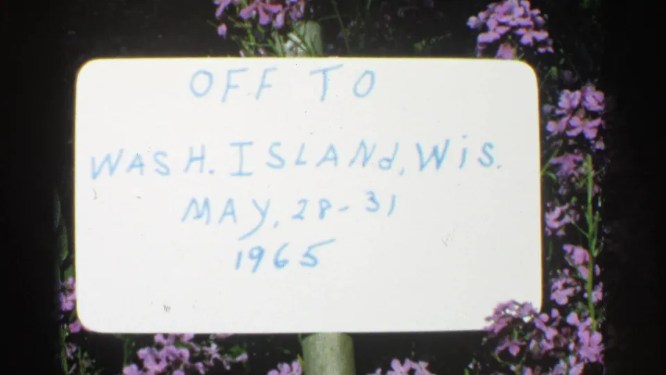 Final frame holds on the white Washington Island, Wisconsin trip sign, surrounded by purple flowers and 8mm film borders.