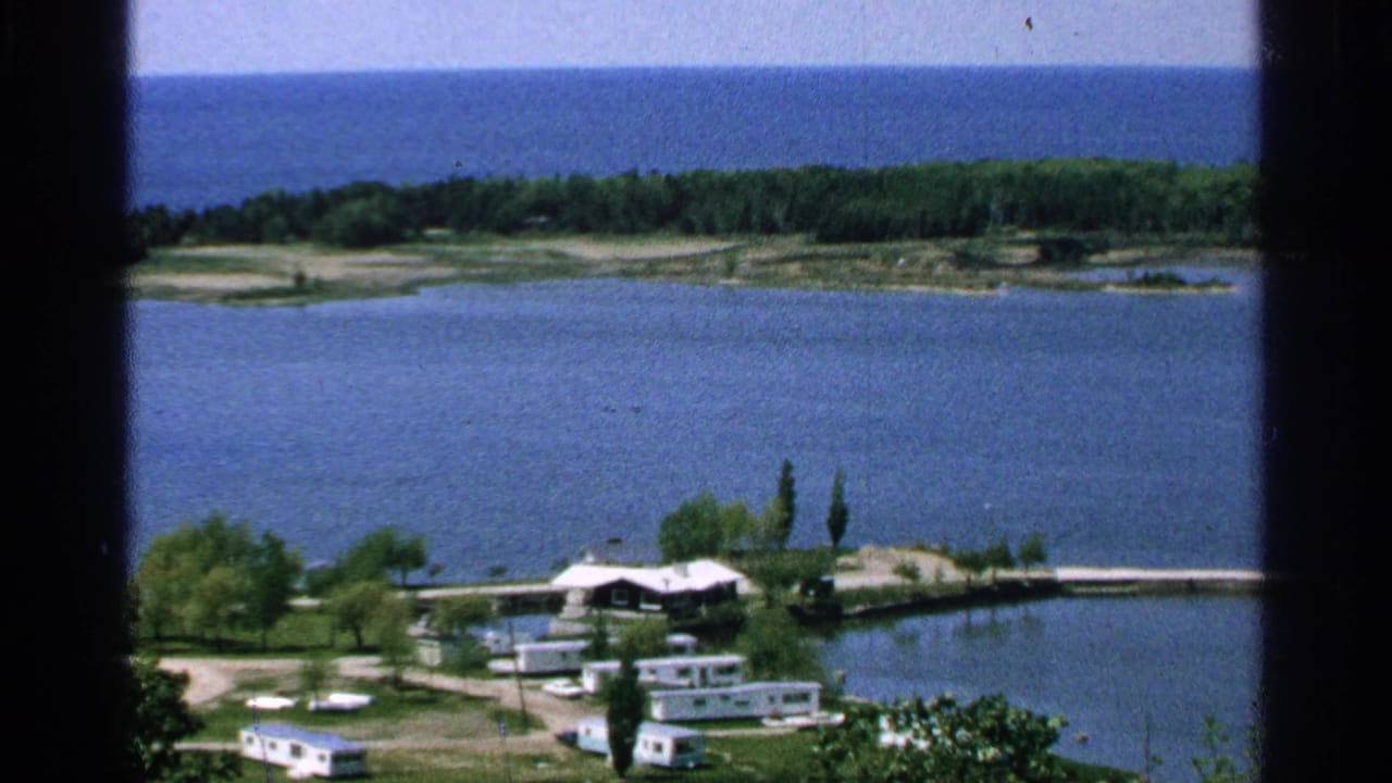 1964 8mm view from Washington Island, Wisconsin, showing lake water, small shore buildings, trees, and a distant wooded island.