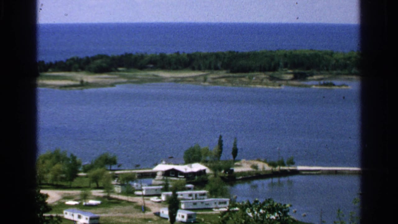 Washington Island lakeshore scene from 1964 with small buildings near the water and forested land beyond the lake.