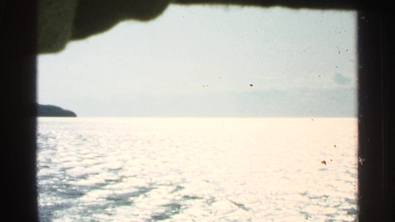 Bright water seen through dark boat-window edges with a distant landform at left.