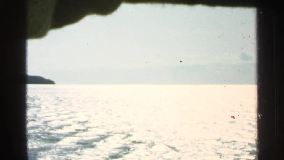 1964 Washington Island boat view across sun-glinting water, framed by dark edges of the vessel and a low distant shore.