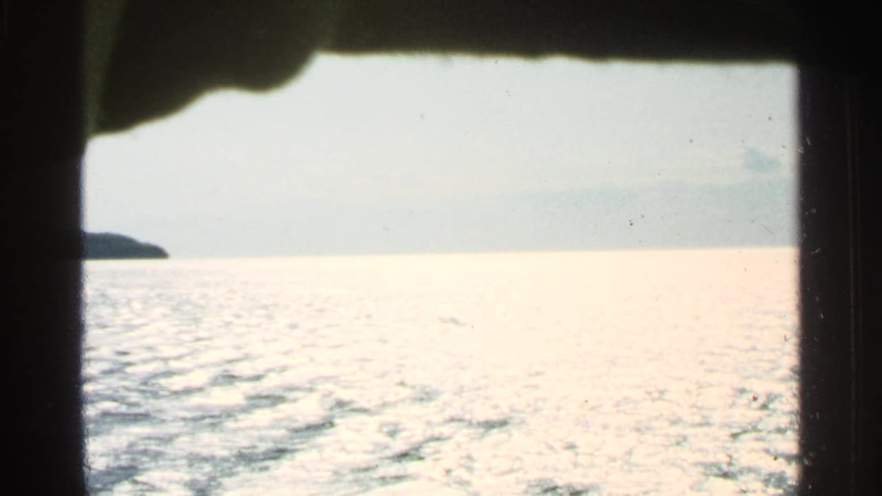 Open water and pale sky framed by dark boat-window edges, with land at the far left.