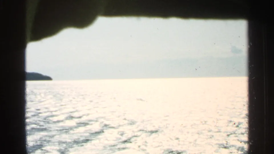 Boat-level view near Washington Island in 1964, showing bright rippled water, pale sky, and a small distant shoreline at left.