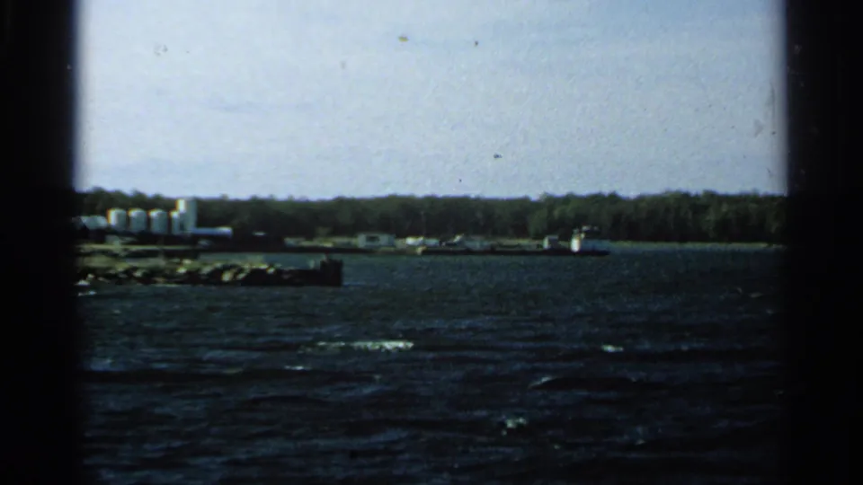 Washington Island shoreline in 1964, showing pale industrial-looking buildings near trees and choppy water from a boat viewpoint.
