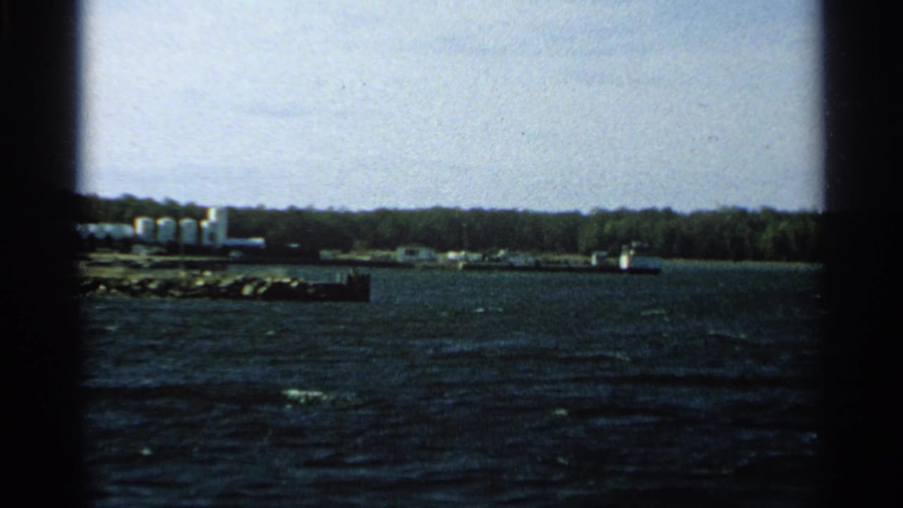 Choppy water with a distant wooded shoreline, white tanks, and a small dock.