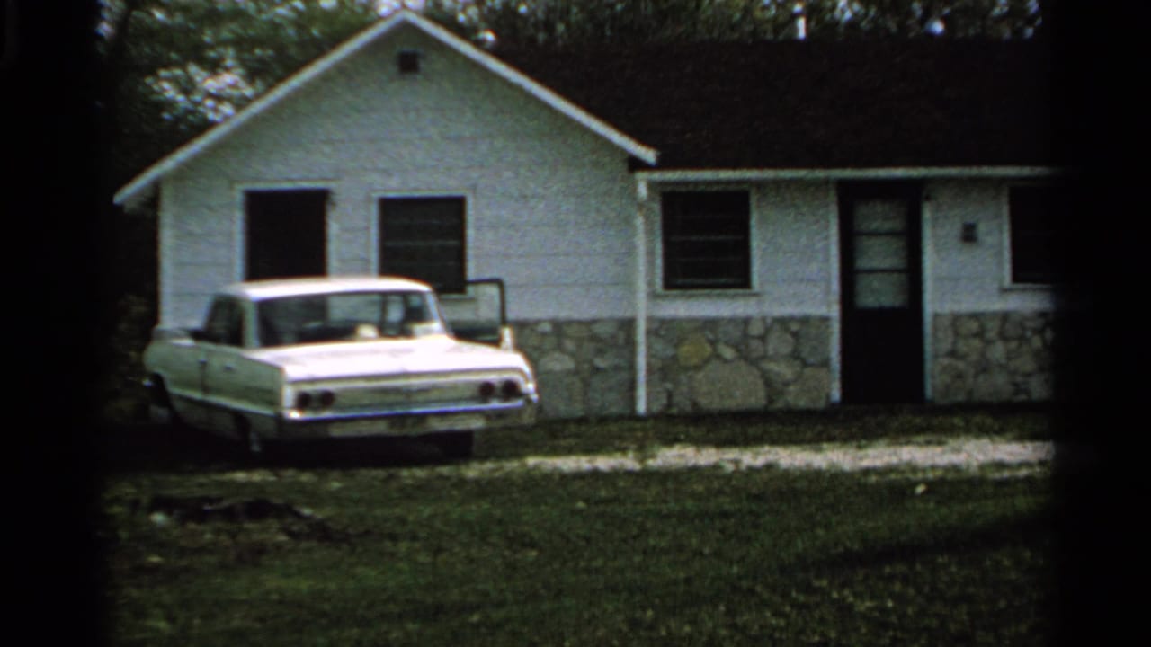 White motel cabin with a stone foundation and a white 1960s sedan parked on grass in Washington Island, Wisconsin.