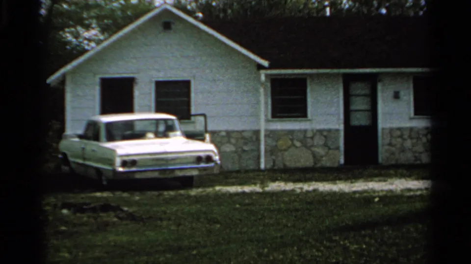 White motel cabin with a stone foundation and a white 1960s sedan parked on grass in Washington Island, Wisconsin.