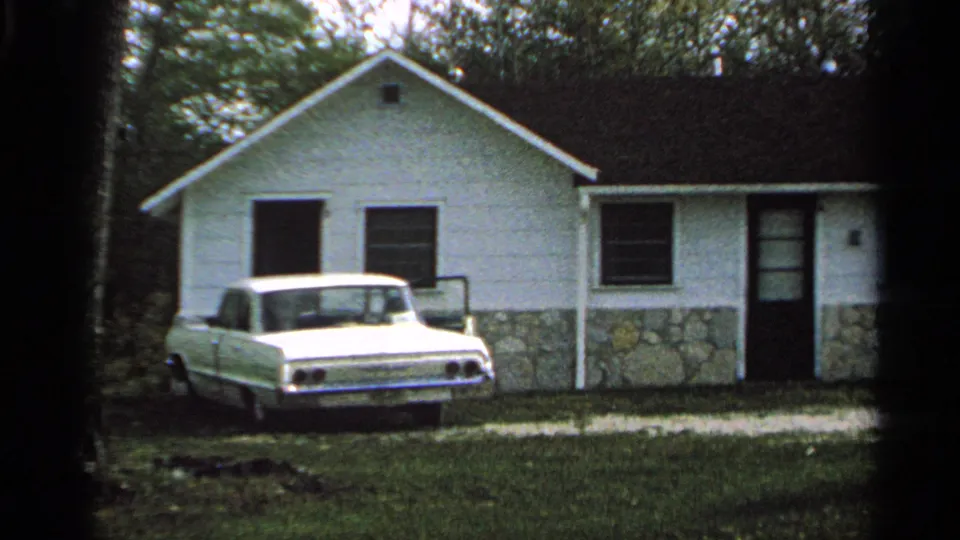 Final view of the Washington Island motel cabin, with a white sedan in front and dark 8mm frame edges around the scene.